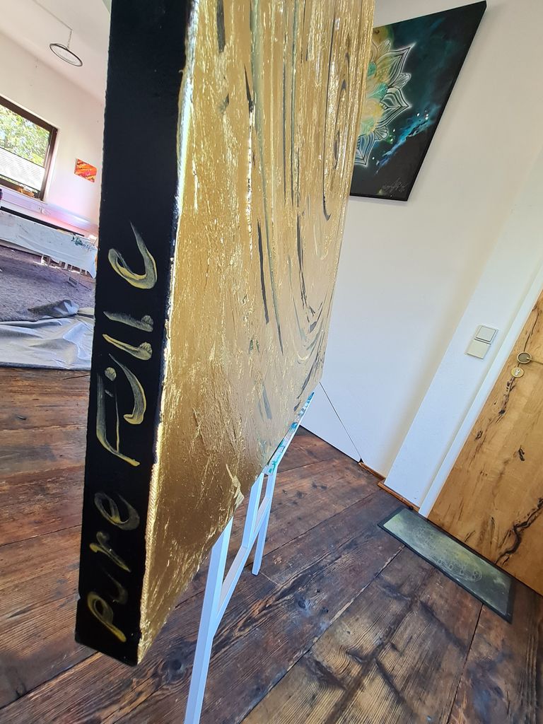Nahaufnahme einer vertikal stehenden, goldfarbenen Leinwand mit der Aufschrift 'Pure Pulse' auf der schwarzen Kante, in einem Innenraum mit Holzboden und weiteren Dekorationen an den Wänden.