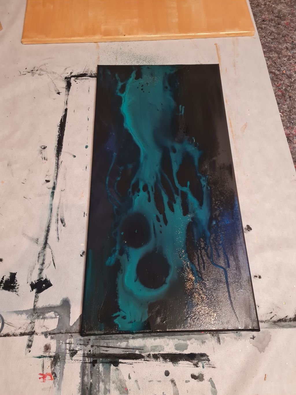 Ein rechteckiges Kunstwerk auf einem mit Farbflecken bedeckten Untergrund, das mit schwarzen und türkisen fließenden Mustern gestaltet ist.