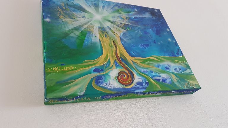 Ein farbenfrohes Gemälde an der Wand zeigt eine strahlende weiße Lichtquelle oberhalb eines spiralförmigen Wurzelsystems vor blau-grünem Hintergrund mit der aufgemalten Botschaft „HEILUNG“ und einem Teil des Schriftzugs „Bewusstsein ist Gesundheit“.