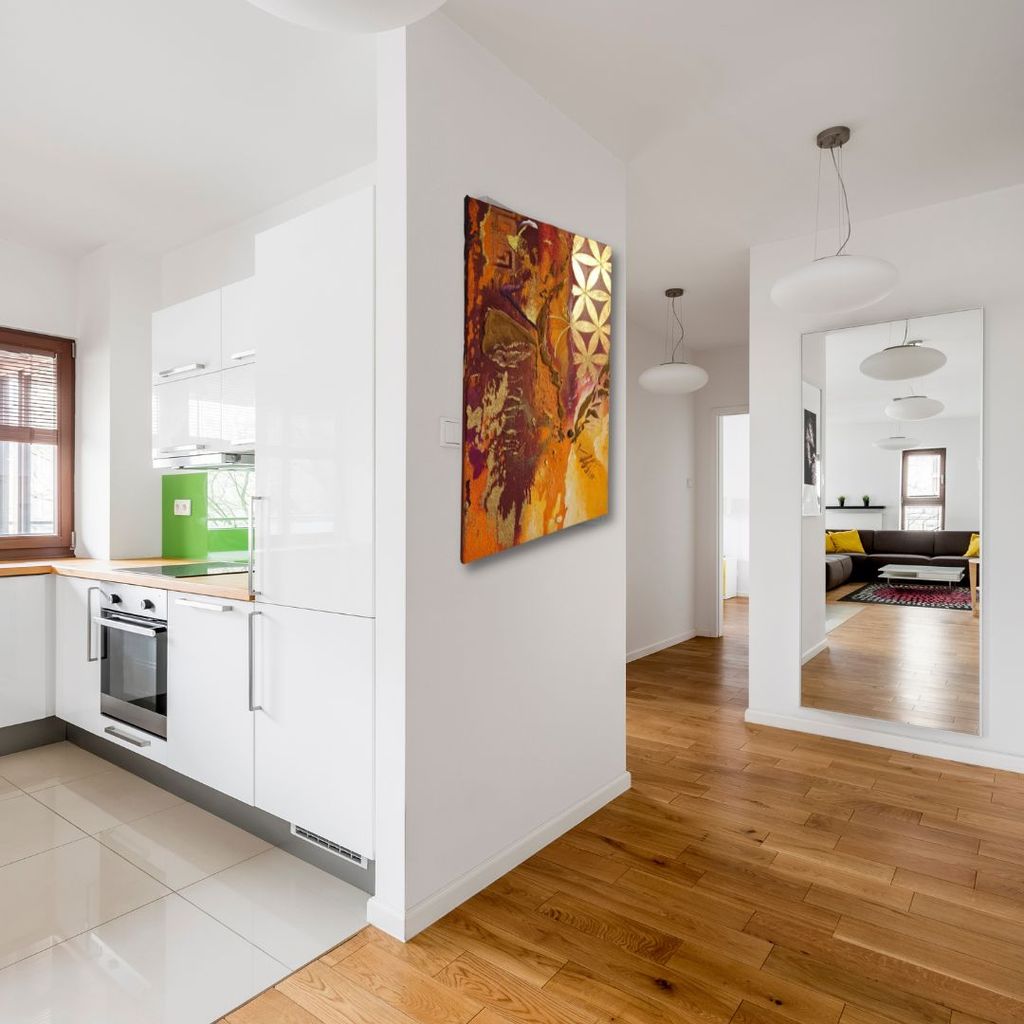Moderner Wohnbereich mit weißer Küchenzeile, künstlerischem Gemälde an der Wand und großem Spiegel, der einen Sitzbereich mit Sofa und Teppich reflektiert.