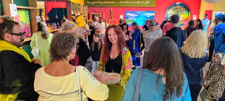 Menschen unterschiedlicher Altersgruppen interagieren und schauen sich in einem bunt dekorierten Raum eine Ausstellung an mit großen Gemälden an den Wänden.