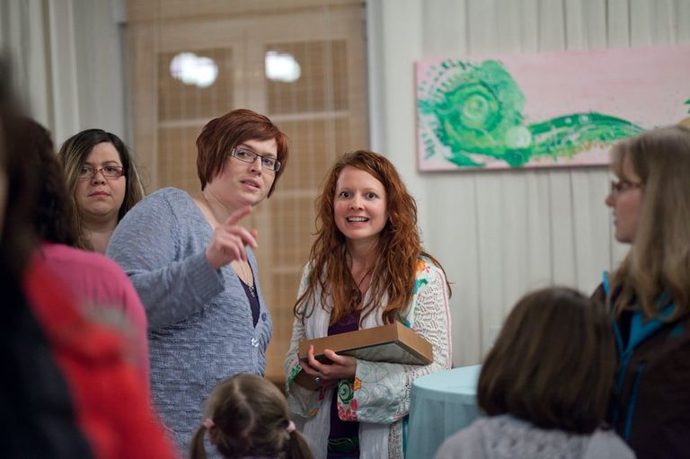 Gruppe von Frauen bei einer Ausstellung oder Veranstaltung, zwei Frauen im Vordergrund unterhalten sich, eine hält ein Buch oder einen Katalog in der Hand.