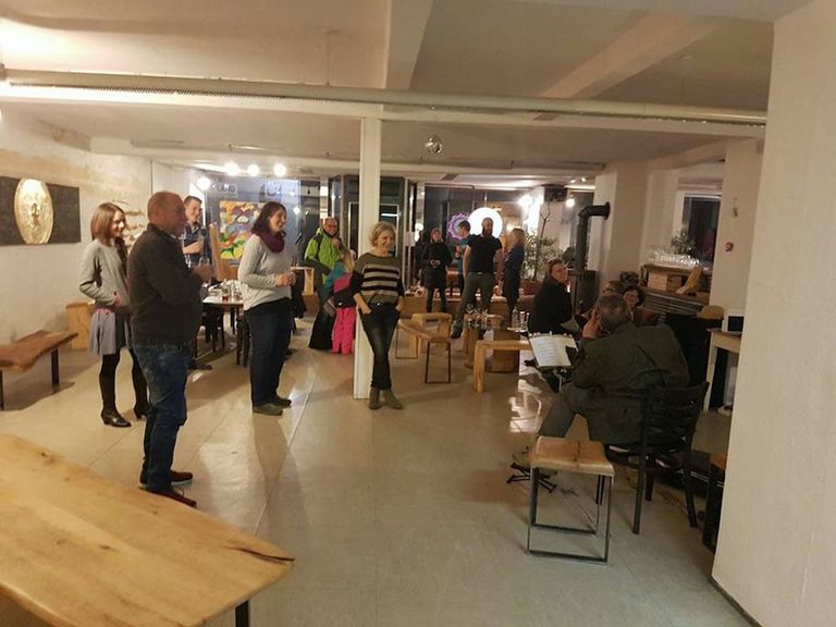 Eine Gruppe von Menschen steht und sitzt in einem gut beleuchteten Raum mit Ausstellungsflächen, auf denen Kunstwerke präsentiert werden.
