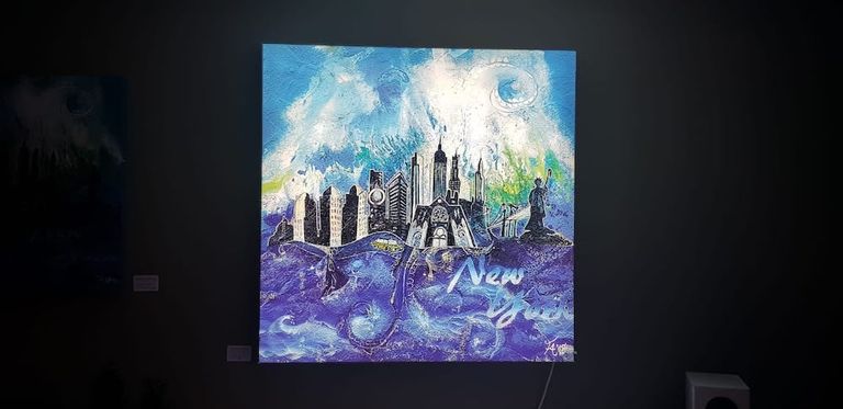 Ein beleuchtetes Gemälde an einer dunklen Wand zeigt eine stilisierte Skyline von New York mit Wolken, Wasser und dem Schriftzug "New York" in Blau- und Weißtönen.