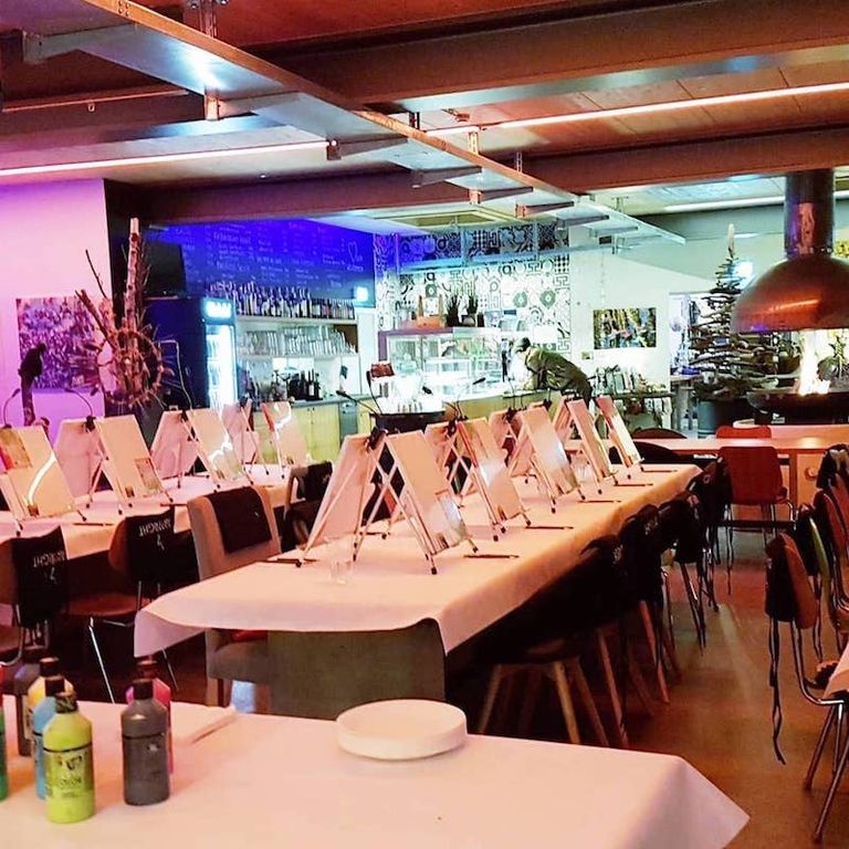 Ein stilvoll eingerichteter Innenraum mit Tischen, auf denen Malerstaffeleien stehen, wahrscheinlich für einen Malkurs oder eine Kunstausstellung, mit einer Bar und dekorativem Hintergrund.