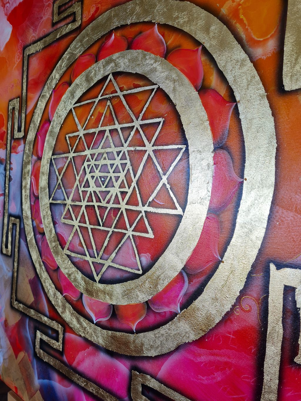 Nahaufnahme eines goldenen Sri Yantra mit roten und orangefarbenen floralen Mustern im Hintergrund.